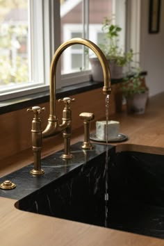 a kitchen sink with gold faucet and black marble countertop in front of a window