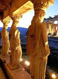 some statues are lit up in front of an old building with columns and lights around them