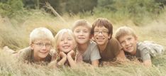 four children laying in tall grass with their hands on each other's heads and smiling