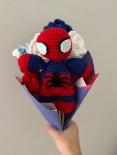 a crocheted stuffed animal is held in a paper bouquet with blue and red ribbon