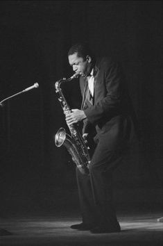 a man in a tuxedo playing a saxophone on stage with a microphone behind him