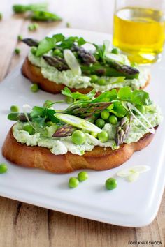 two pieces of bread topped with green veggies and pea sauce on a white plate