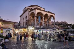 people are walking around in front of an old building with arches on the roof and shops below