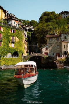 a small boat is in the water near some buildings and green plants on the hillside