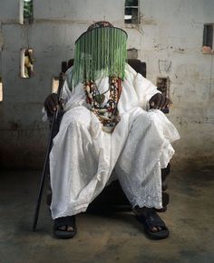 an old man sitting in a chair with beads on his head