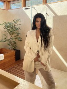 a woman standing in front of a shower wearing a white blazer and khaki pants