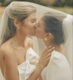 two brides kissing each other in front of a veil on their wedding day at the same time