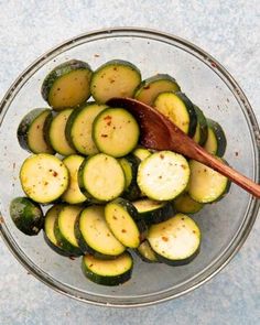 a glass bowl filled with sliced cucumbers and a wooden spoon