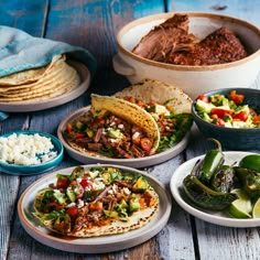 several plates of food are arranged on a wooden table, including tortillas and vegetables