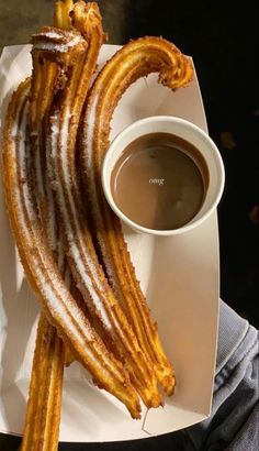 some churros on a white plate with a cup of coffee