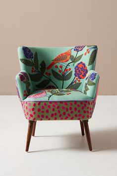 an upholstered chair with colorful flowers and birds on the back, against a beige background