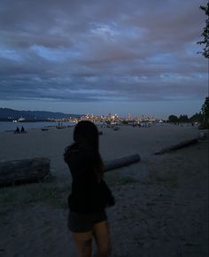 a woman standing on top of a sandy beach next to the ocean under a cloudy sky