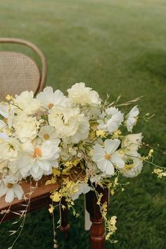 a bouquet of white flowers sitting on top of a wooden table next to a chair