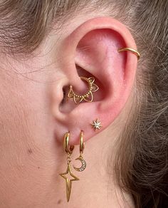 a woman wearing gold ear cuffs with stars and crescents on them, while she is looking at the side of her ear