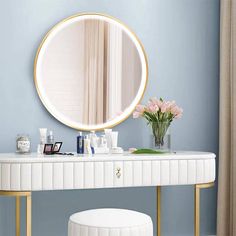 a white vanity with a round mirror above it and pink flowers in a vase on the counter