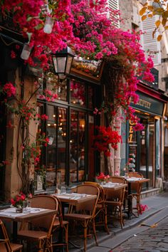 tables and chairs are lined up in front of a restaurant with pink flowers hanging from the windows