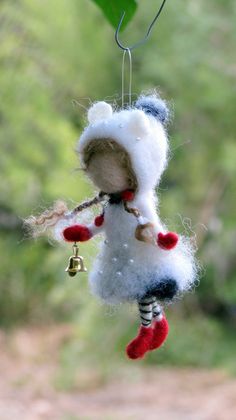 a small stuffed animal hanging from a hook on a tree branch with a bell attached to it