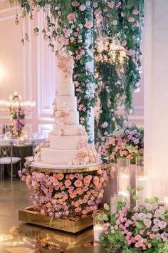 a wedding cake is surrounded by pink flowers and greenery at the end of a table