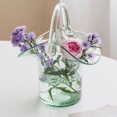 purple flowers in a clear glass vase on a white table with a card and pen