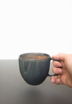 a hand holding a black coffee cup on top of a gray table next to a white wall