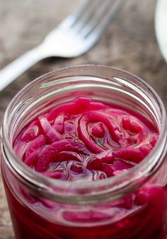 a jar filled with red liquid sitting on top of a wooden table next to a knife and fork