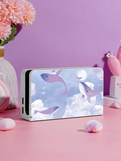 a pink table topped with two cell phones next to vases filled with flowers and clouds