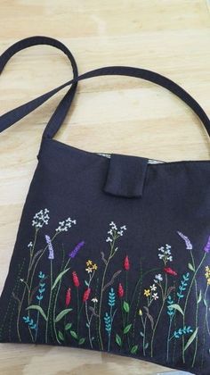 a black purse with flowers on it sitting on top of a wooden table next to a pair of scissors