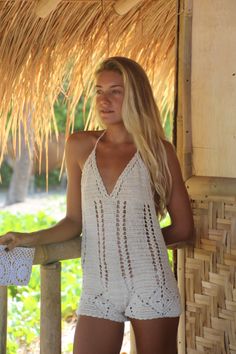 a woman standing in front of a straw hut wearing white crochet shorts and a tank top