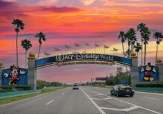 the entrance to walt world at sunset with cars driving under it and palm trees in the background