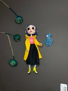 the doll is wearing a yellow coat and black dress with blue hair, standing in front of some beads