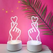 two illuminated hands holding hearts on top of a table next to a palm leaf and pink wall