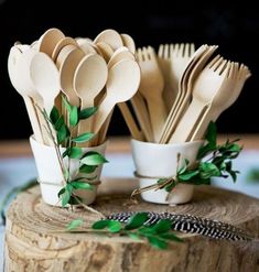 wooden spoons and forks are arranged in cups on a tree stump with greenery