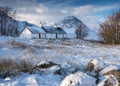 a house in the middle of a field with snow on it and mountains in the background