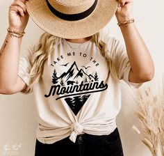 a woman wearing a hat and t - shirt with the mountains on it is covering her eyes