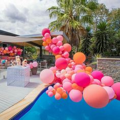 balloons are floating in the air near a pool with tables and chairs set up for an outdoor party