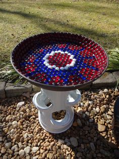 a red, white and blue glass bowl sitting on top of a rock garden bed