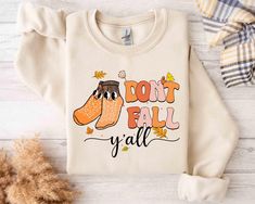 a sweater with the words don't fall y'all on it next to some autumn decorations