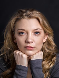 a woman with long blonde hair and blue eyes posing for a studio photo in front of a black background