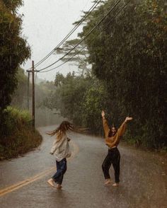 two people jumping in the rain on a road with trees and telephone wires above them