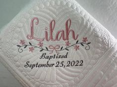 a close up of a quilt with the name lilly printed on it and flowers in pink