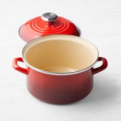 two red pots sitting next to each other on a white counter top with a silver lid