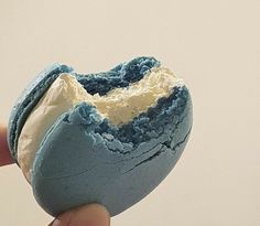 a hand holding a blue and white doughnut with icing on it's side