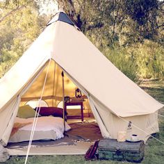 a tent with a bed in it sitting on top of a grass covered field next to trees