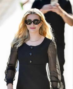 a woman in black dress and sunglasses walking down the street