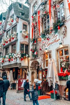 people are walking down the cobblestone street in an old european town decorated for christmas