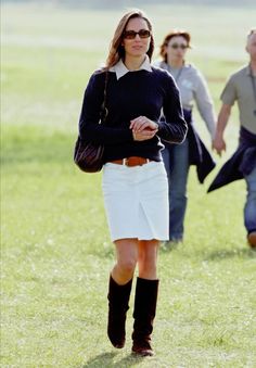 a woman walking across a lush green field next to two women in short skirts and knee high boots