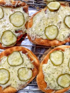 four pizzas with cheese and cucumbers on them sitting on a cooling rack