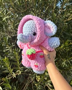 a hand holding a pink crocheted stuffed animal with a strawberry on it's chest