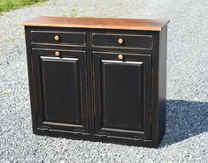 a black cabinet with two doors and drawers on gravel ground next to grass, in front of grassy area