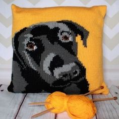 a yellow pillow with a black dog on it and two knitting needles next to it